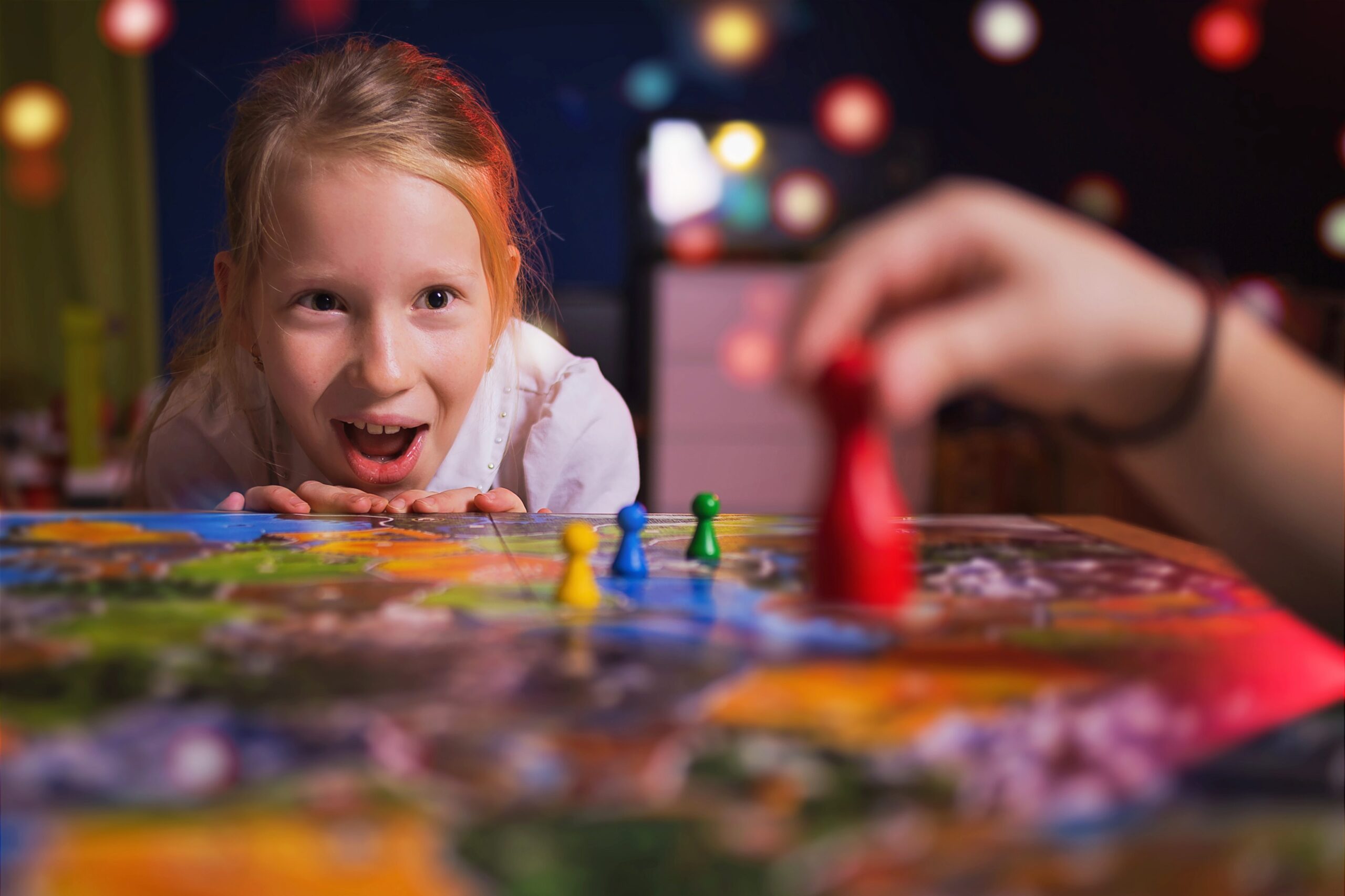 A young girl gets excited as another person moves their game piece onto a board.